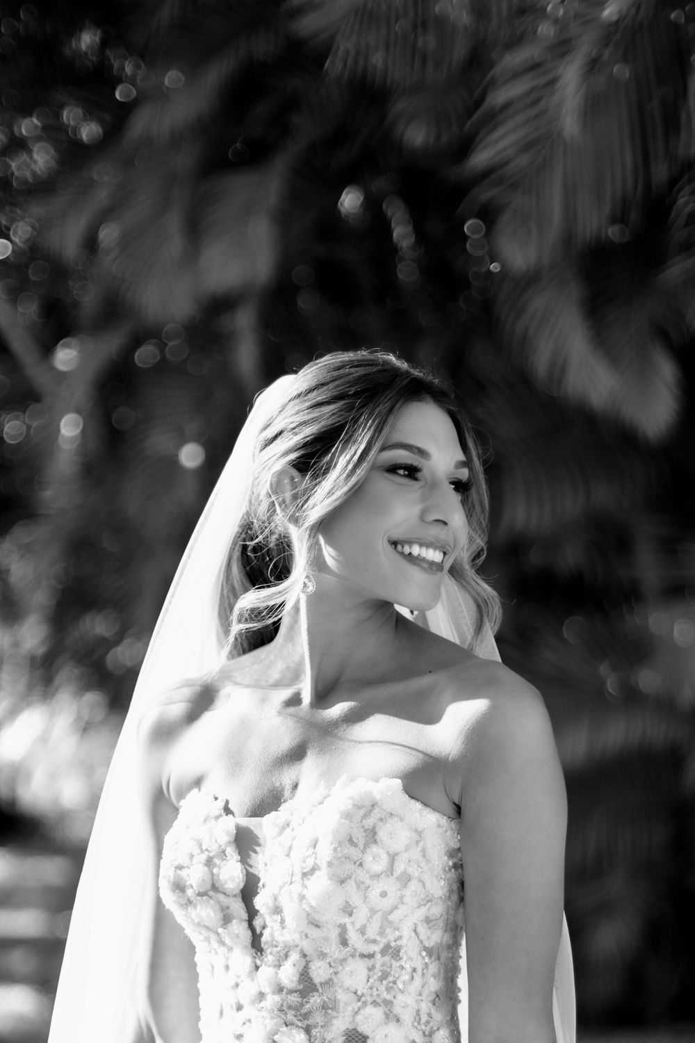 Black and white portrait series showing a joyful bride in a lace wedding dress with veil against a blurred background.