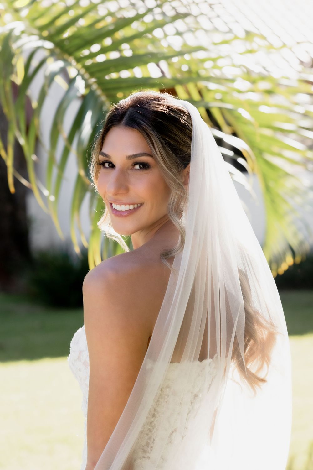 Candid series of a bride in a strapless lace gown and veil posing outdoors with palm trees in the background.