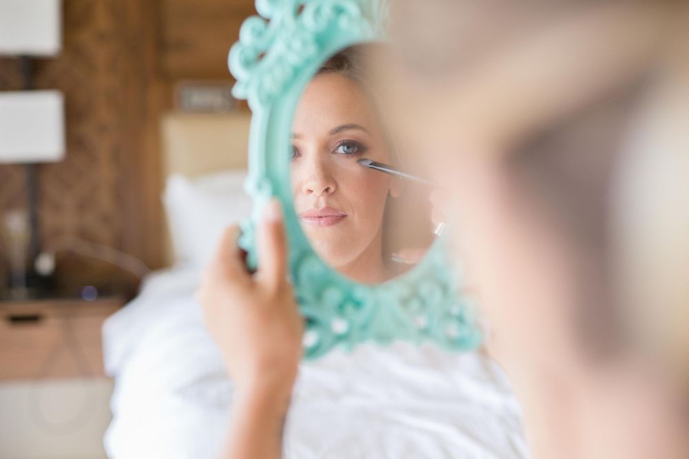 A person wearing a mint green hijab and white dress smiles while getting ready for a special occasion.