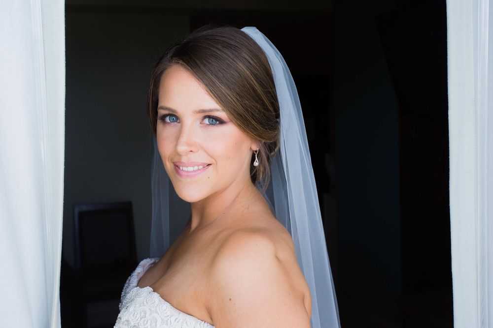 Bride in a white wedding gown and veil smiles during her wedding day photoshoot.