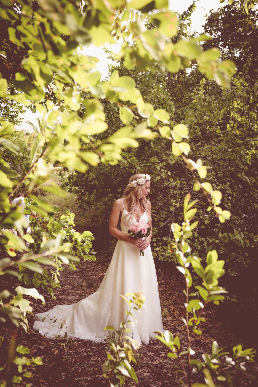 A romantic garden wedding scene with sunlit foliage framing a flowing white dress among lush greenery.