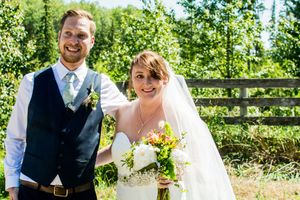 Couple shares romantic moment in front of rustic wooden fence surrounded by greenery.