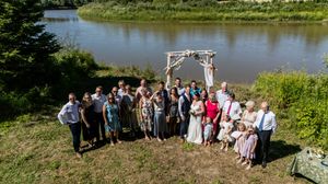 Wedding guests line up for a panoramic group photo by a scenic lakeside setting.