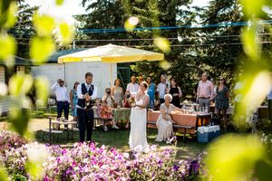 An outdoor reception area decorated with pink flowers and yellow umbrellas under tall evergreen trees.