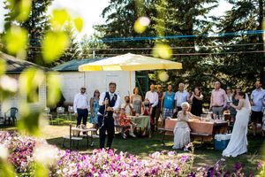 Outdoor wedding reception setup with string lights and pink flowers under tall evergreen trees.