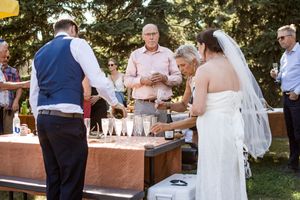 Wedding guests gather around a rustic wooden bar during an outdoor garden reception celebration.