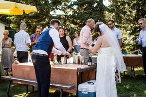 Wedding guests gather around rustic wooden tables at an outdoor garden reception under string lights and trees.