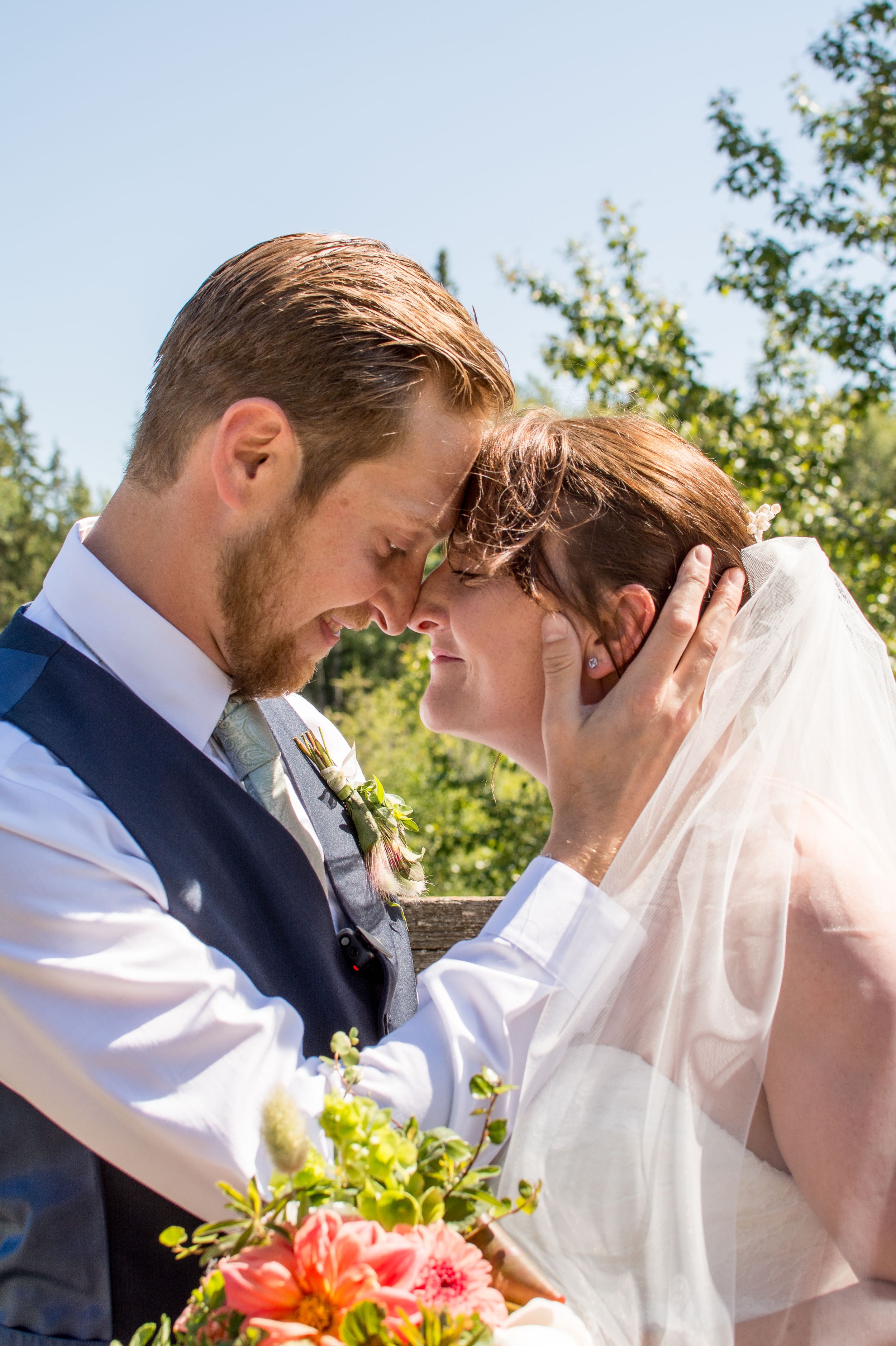 Intimate wedding moment captured outdoors with delicate veil and coral bouquet details.
