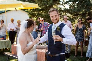 A couple shares a celebratory toast at an outdoor summer wedding reception with guests in the background.