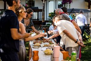 Wedding guests gather around tables at an outdoor reception preparing food and drinks together.