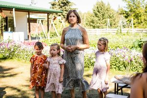 A group gathers outdoors on a sunny day near a garden with flowers and trees in the background.