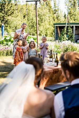 Wedding guests celebrate joyfully at an outdoor summer reception surrounded by trees and sunlight.