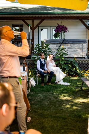 A casual outdoor wedding reception with guests gathered on a sunny lawn near a white house.