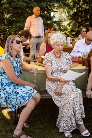 Group of guests in summer dresses enjoying conversation at outdoor garden party.