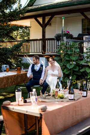 An outdoor wedding bar setup with bottles and glasses on a long table draped in brown cloth.