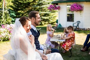 Wedding celebration at white farmhouse with hanging flower baskets and outdoor seating.