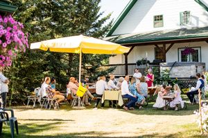 Wedding guests gather at outdoor reception tables under yellow umbrellas on a sunny summer day.