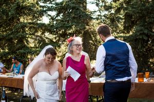 Wedding guests mingle and socialize at outdoor reception tables surrounded by lush greenery.