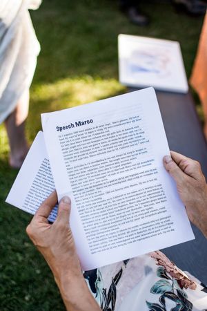 Wedding guests reading ceremony programs outdoors on a sunny day.