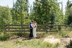 A couple poses together in a rustic outdoor setting with tall trees and natural greenery in the background.