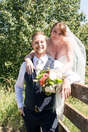 Wedding couple poses together by rustic fence during outdoor summer celebration.