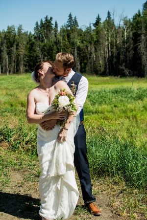 Wedding couple embracing in a sunny meadow surrounded by evergreen trees.
