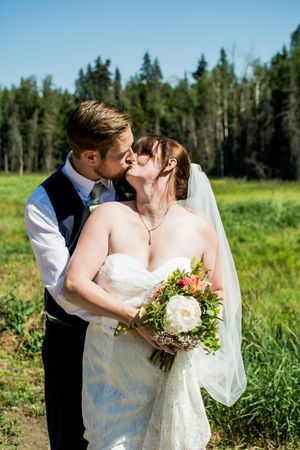 Wedding couple shares intimate kisses in a meadow with evergreen trees in the background.