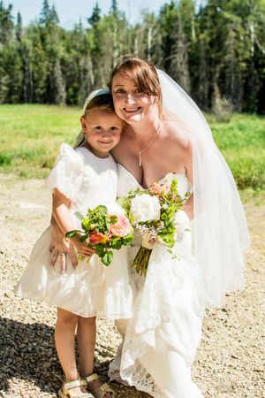 Bride in white dress sharing a tender moment with a young child outdoors.