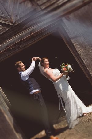 Artistic wedding photo captured through rustic wooden beams in dramatic lighting.