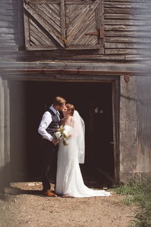 A romantic wedding couple shares an intimate moment in the doorway of a rustic wooden barn.