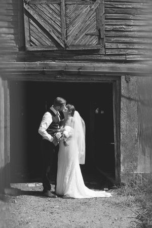A wedding couple poses for romantic photos in front of a rustic wooden barn structure.
