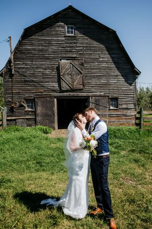 A wedding couple shares romantic moments in front of a rustic wooden barn.