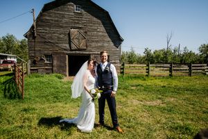 A wedding couple poses for photos in front of a vintage barn in a pastoral setting.