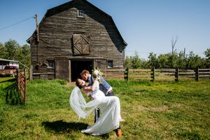 Wedding couple poses in front of an old wooden barn on a grassy hillside.