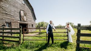 Rustic barn and wooden fence frame a countryside wedding scene.