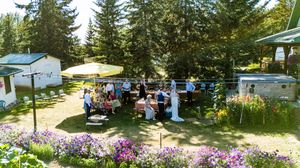 Panoramic view of an outdoor wedding venue with pine trees and blue umbrellas.