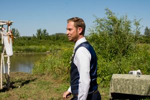 A groom in formal attire poses near a waterfront setting on his wedding day.