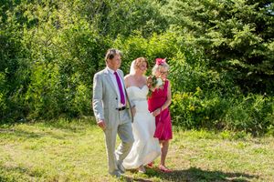Wedding guests in colorful attire gather on a sunny lawn surrounded by greenery.