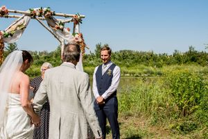 A wedding ceremony takes place in a sunny field with guests gathered around.