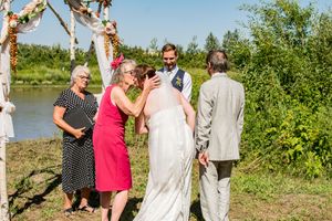 Wedding guests gather outdoors near trees and water for a celebration.
