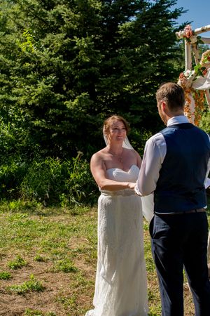 A couple in wedding attire dances together outdoors with green trees in the background.
