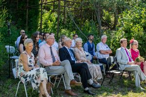 Wedding guests seated in white chairs watching a ceremony in a lush garden setting.