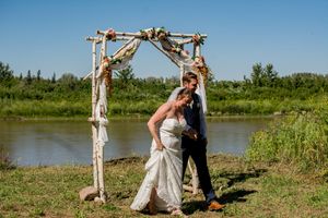 A wedding ceremony takes place by a serene lake with a handmade wooden arch and natural surroundings.