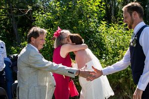 Wedding party members greet each other outdoors during a summer celebration.