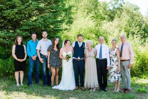 Panoramic group photo of wedding party lined up outdoors against green summer landscape.