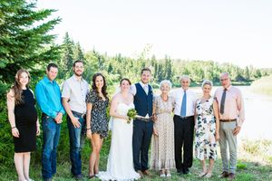 Wedding party and guests pose for a group photo in front of evergreen trees.