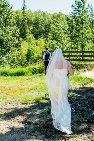 A flowing white wedding dress moves through a scenic natural path surrounded by green trees.