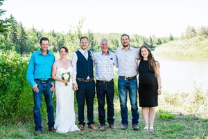 Wedding party members pose together by a lake with trees and natural scenery in the background.