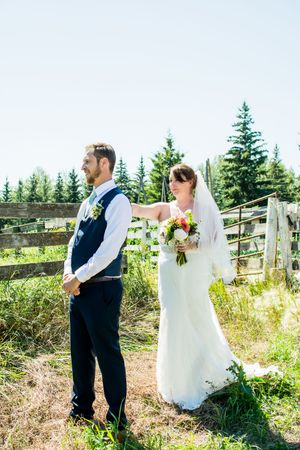 Wedding couple poses in front of evergreen trees on a sunny hillside.