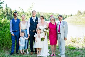 Wedding party members pose together by a lake on a bright summer day.